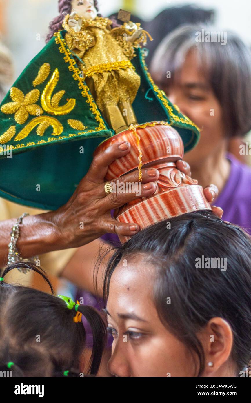 Ein Bild des Sto. Niño wird als Segen in der Ibajay Kirche in Aklan, Philippinen, während eines religiösen Rituals auf dem Kopf eines Gläubigen platziert Stockfoto