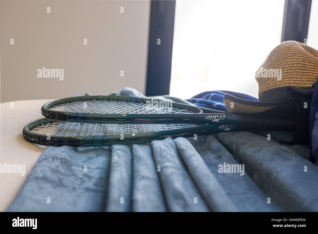 Zwei Tennisschläger und ein Strohhut auf einem gemütlichen Bett, was auf einen aktiven und stilvollen Lebensstil hinweist. Stockfoto