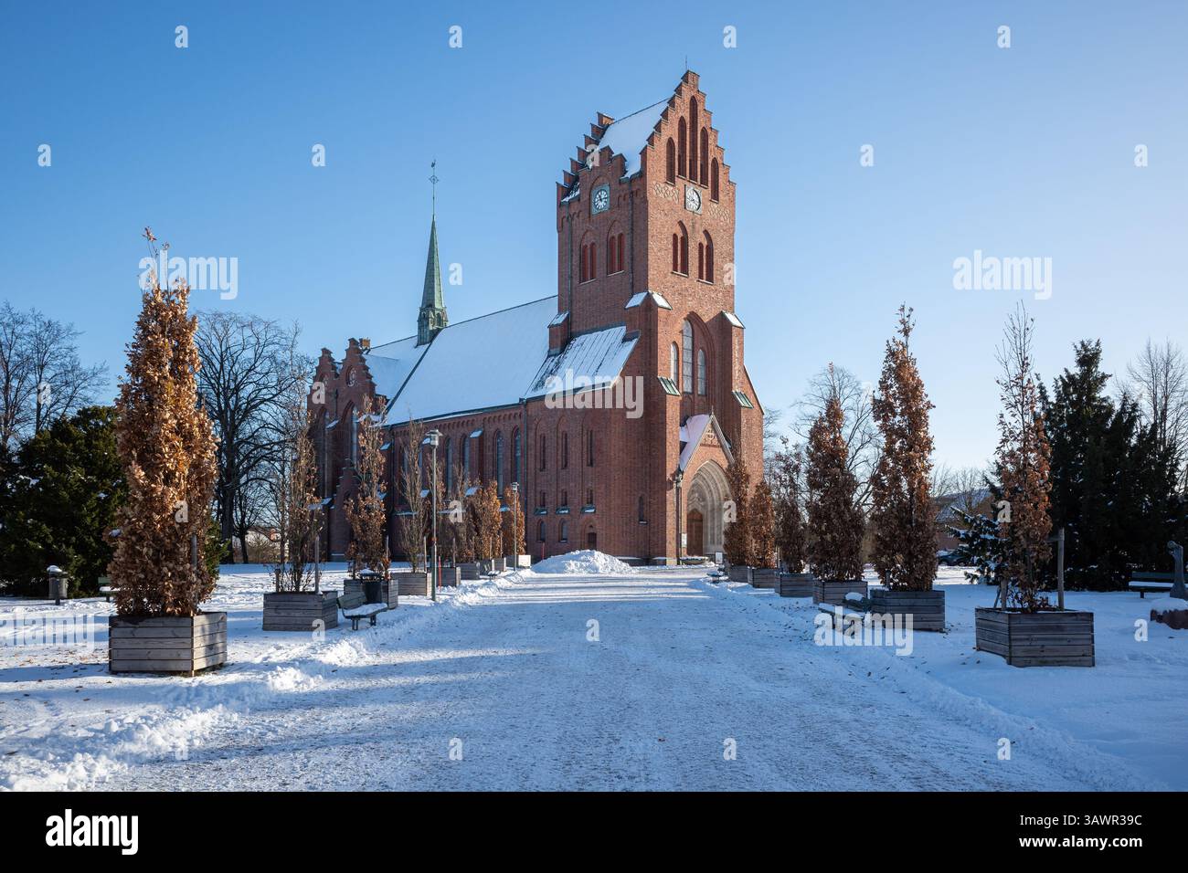 Eine majestätische Ziegelkathedrale in Haessleholm, Schweden, steht hoch unter einer verschneiten Decke, eingerahmt von kargen Bäumen an einem frischen Wintertag. Stockfoto