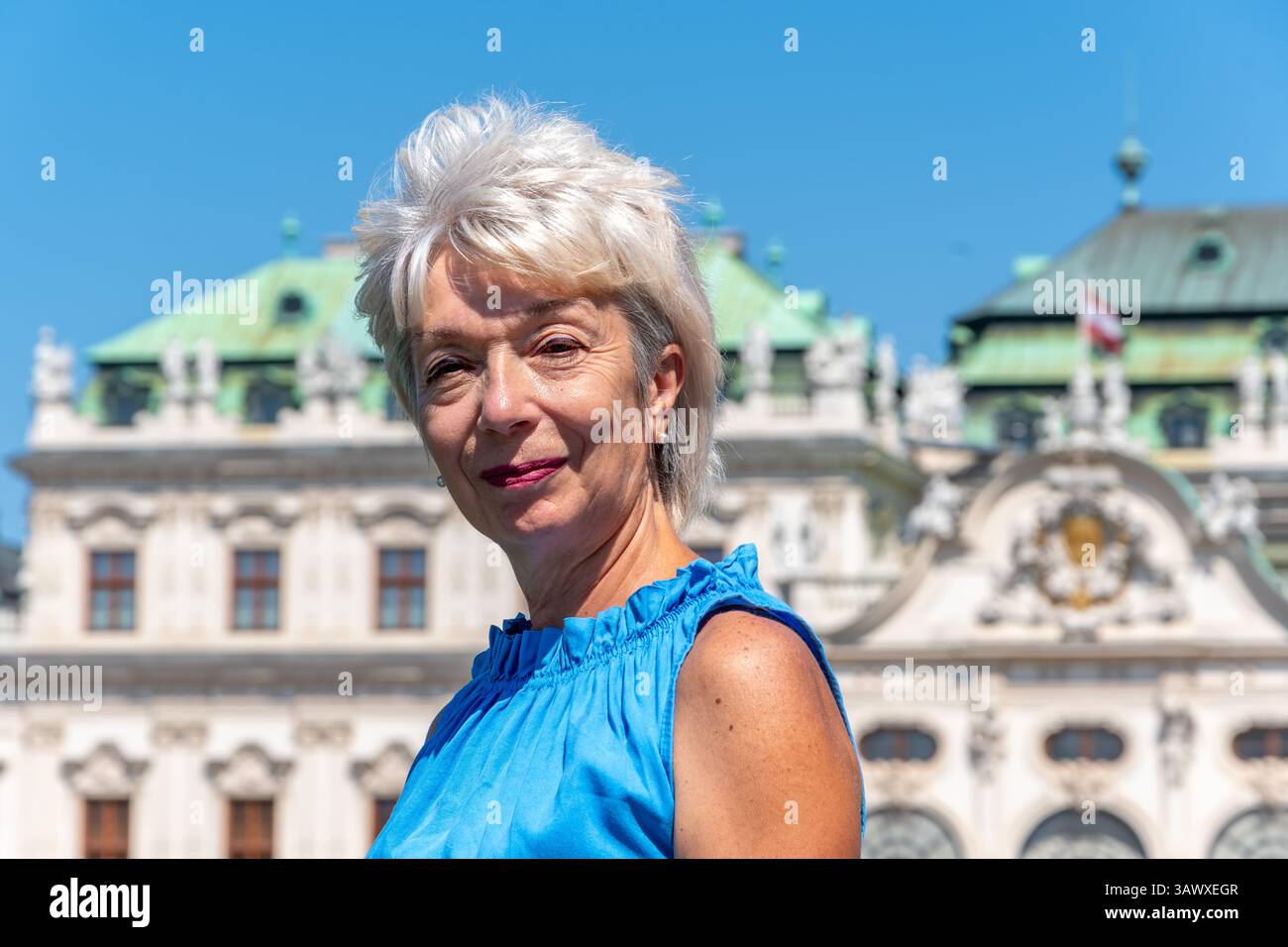 Eine 65-70-jährige Frau mit kurzen blonden Haaren in einem hellblauen Kleid vor dem Hintergrund eines alten Gebäudes Stockfoto