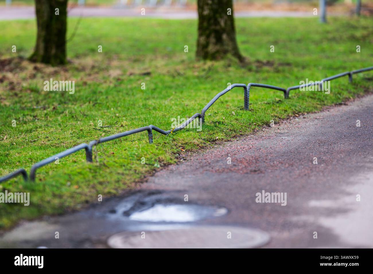 Gebogene Metallbarriere entlang grasbewachsener Straßenränder Stockfoto