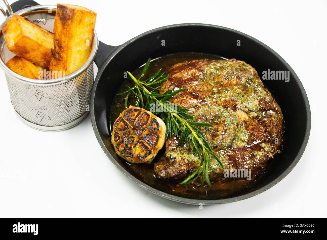 Gegrilltes Rinderrib Eye Steak mit Butter Knoblauch und Rosmarin in einer gusseisernen Pfanne mit weißem Hintergrund Stockfoto