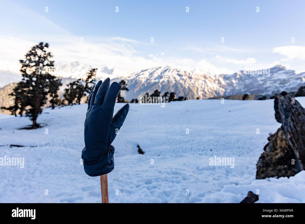 Isolierte Handschuhe, die am Wanderstock gehalten werden, mit atemberaubendem Blick auf die snowcap-Bergkette werden beim Chandrashila-Trek Tungnath Chopta uttarak aufgenommen Stockfoto