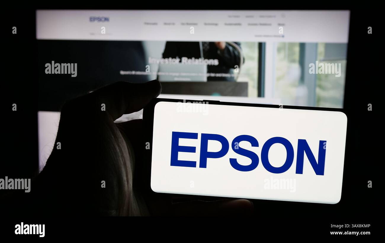 In dieser Abbildung hält eine Person ein Mobiltelefon mit dem Logo des Elektronikunternehmens Seiko Epson Corporation auf dem Bildschirm vor der Webseite. Stockfoto