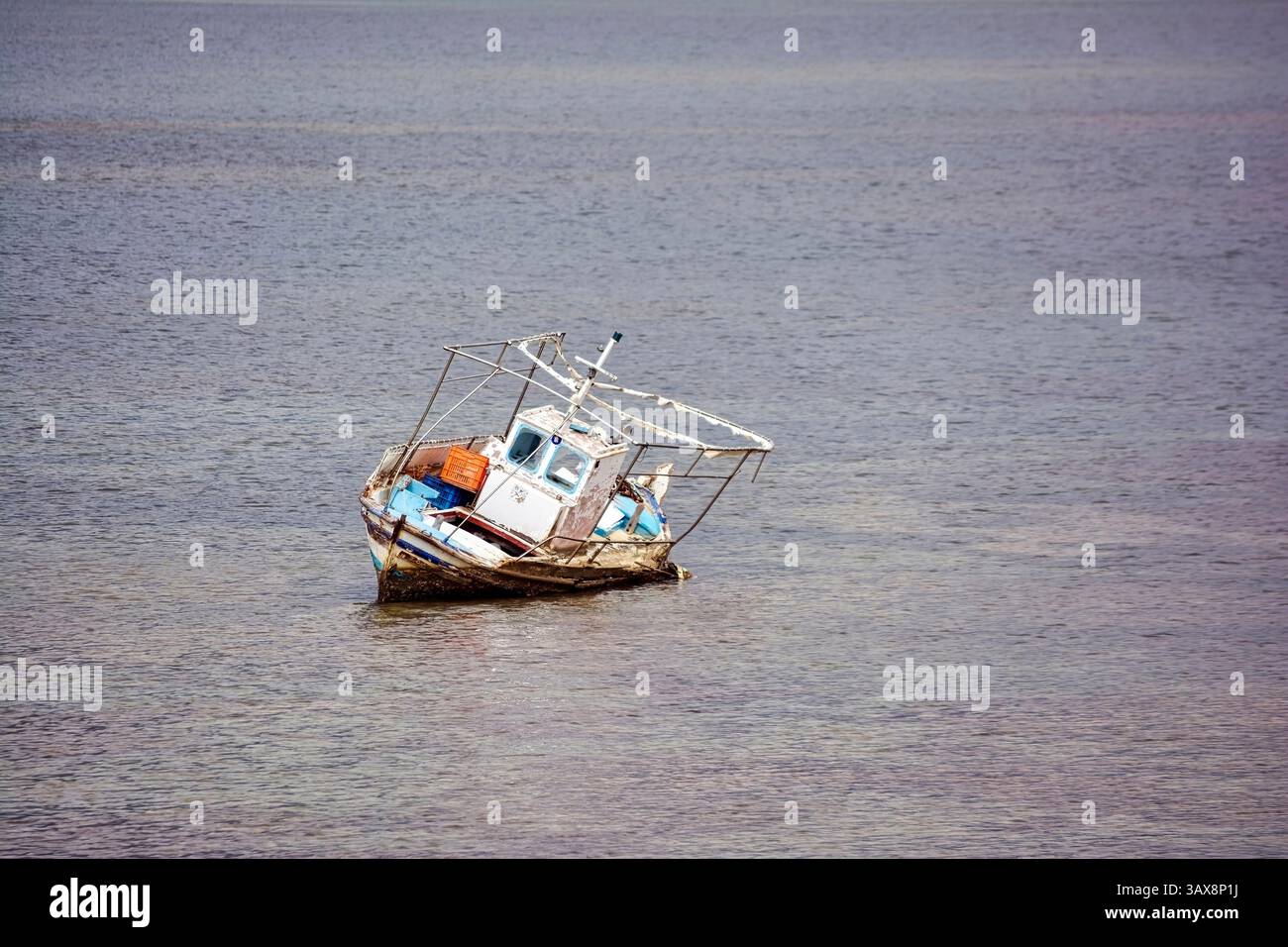 Das alte, geneigte Fischerboot tauchte teilweise in flaches Wasser im Vourkari Wetland ein und schuf eine Szene des Verfalls und der ruhigen Einsamkeit. Stockfoto