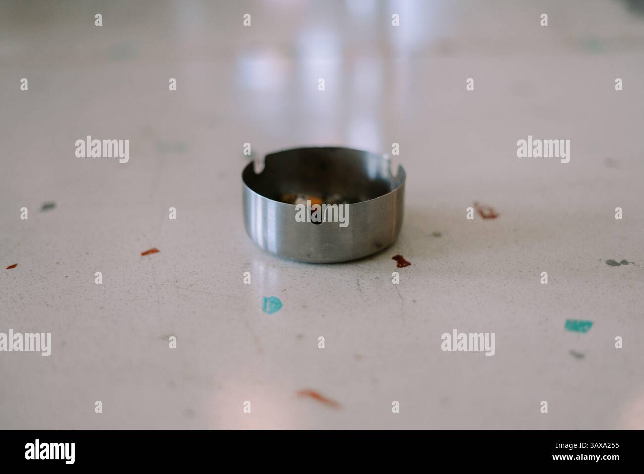 Nahaufnahme eines Aschenbechers aus Metall mit Zigarettenkippen auf einer gesprenkelten Oberfläche, die Rauchen oder sucht darstellen. Stockfoto