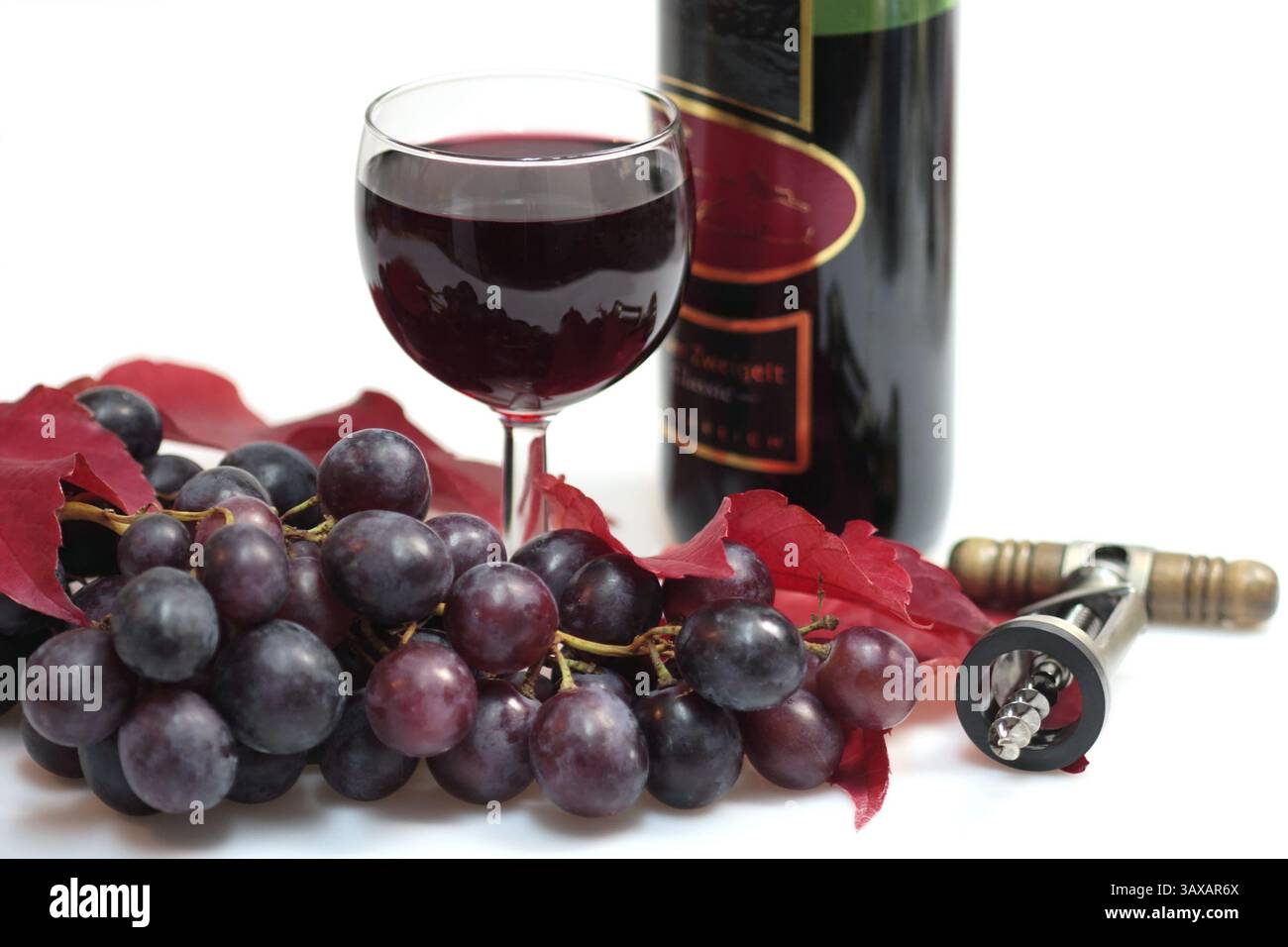 Rotwein in einem Glas mit Trauben, Weinblättern, Weinflasche und Korkenzieher auf weißem Hintergrund Stockfoto