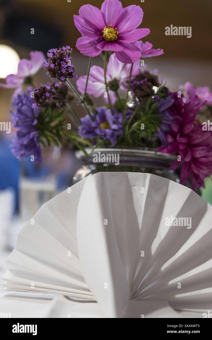 Gefaltete weiße Stoffserviette und bunter Blumenstrauß als Tischdekoration Stockfoto