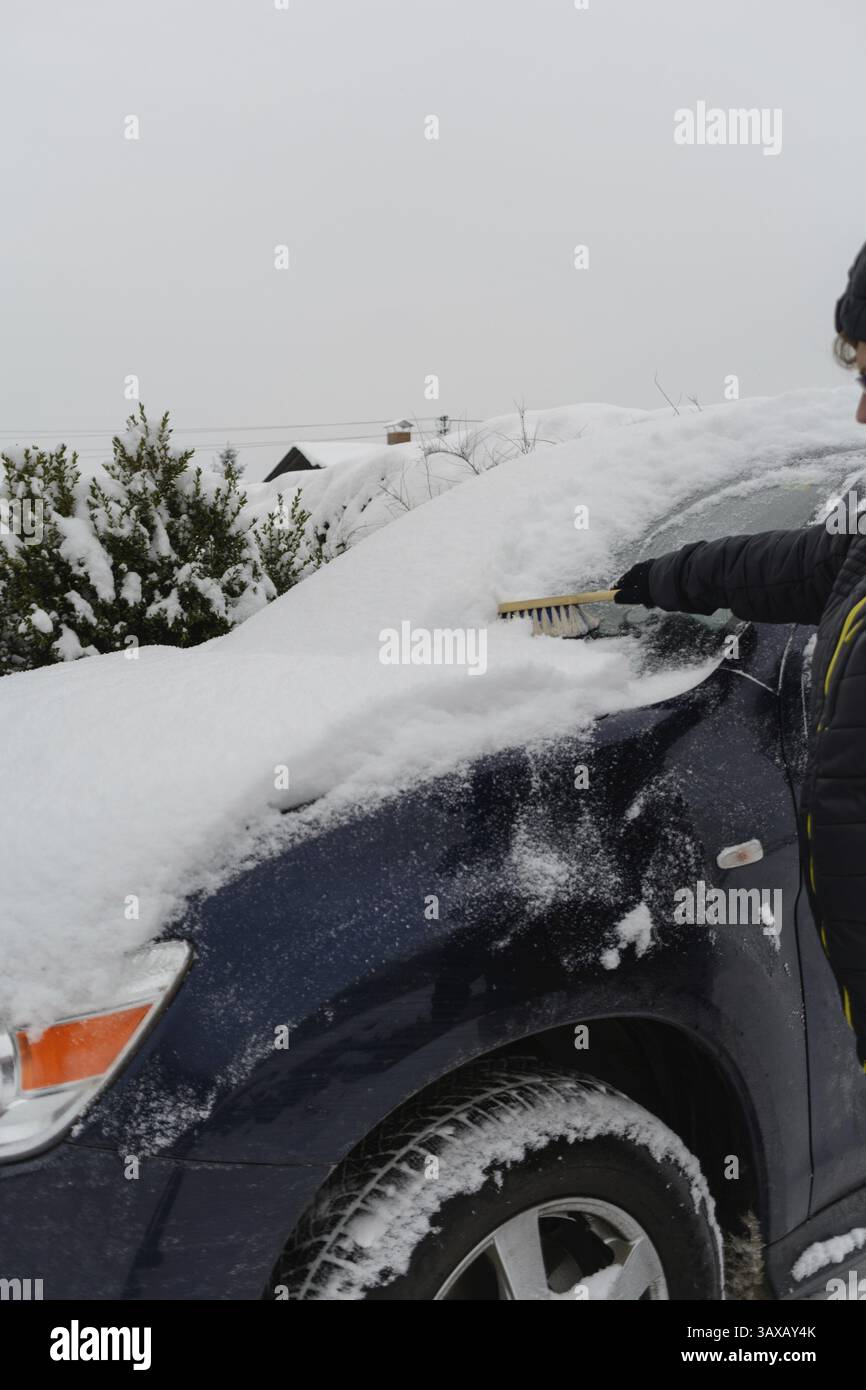 Der Fahrer fegt Schnee von ihrem Auto mit einem Schneebesen Stockfoto