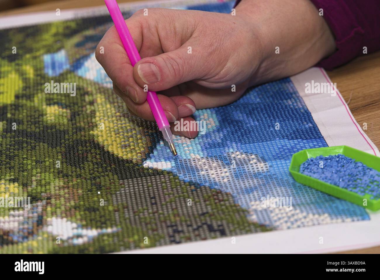 Hand mit Applikator, um ein Diamantgemälde zu erstellen – Farbcodierung in Nahaufnahme Stockfoto