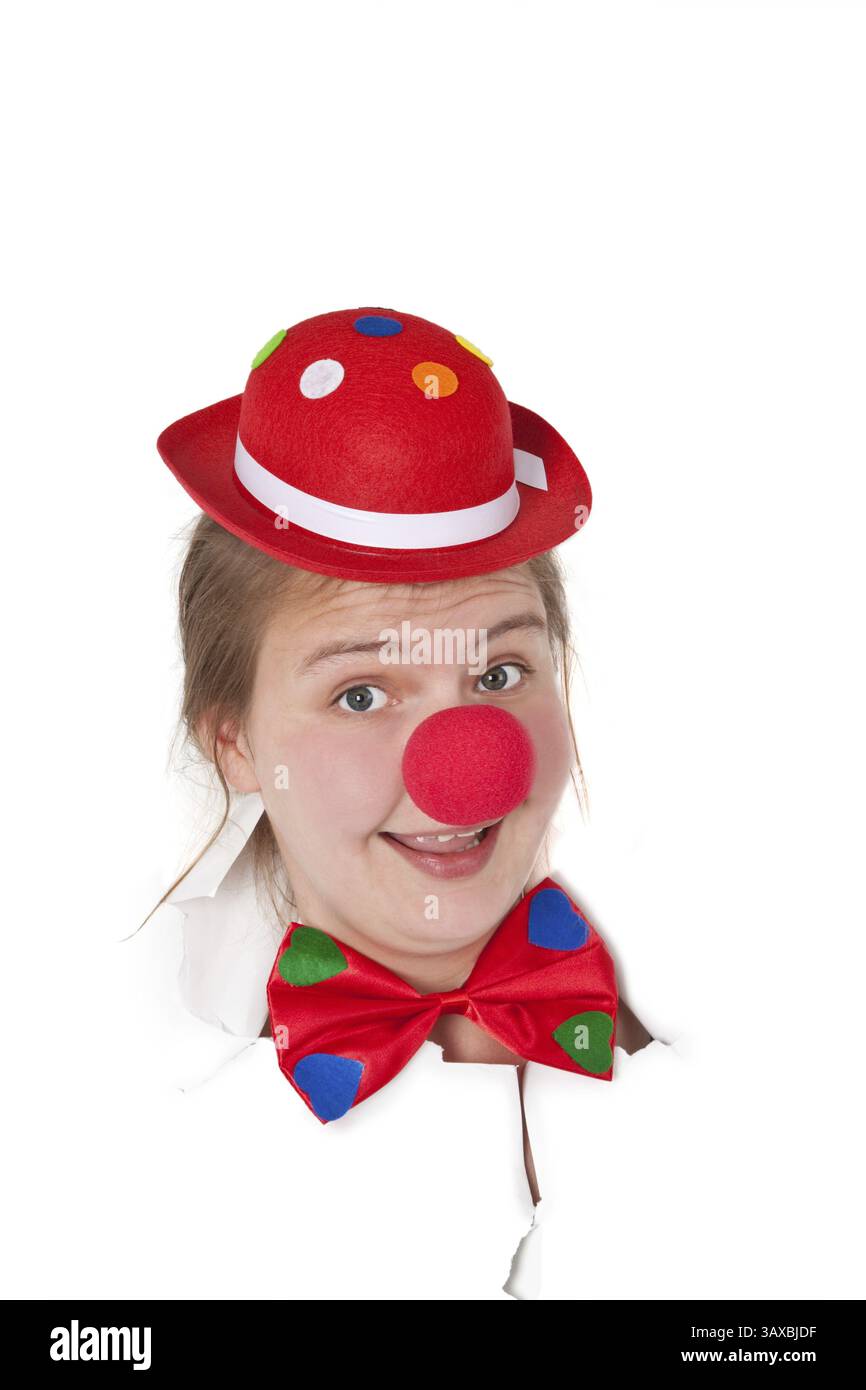 Eine junge Frau mit Clownhut und roter Nase schaut durch ein Loch in der Zeitung Stockfoto