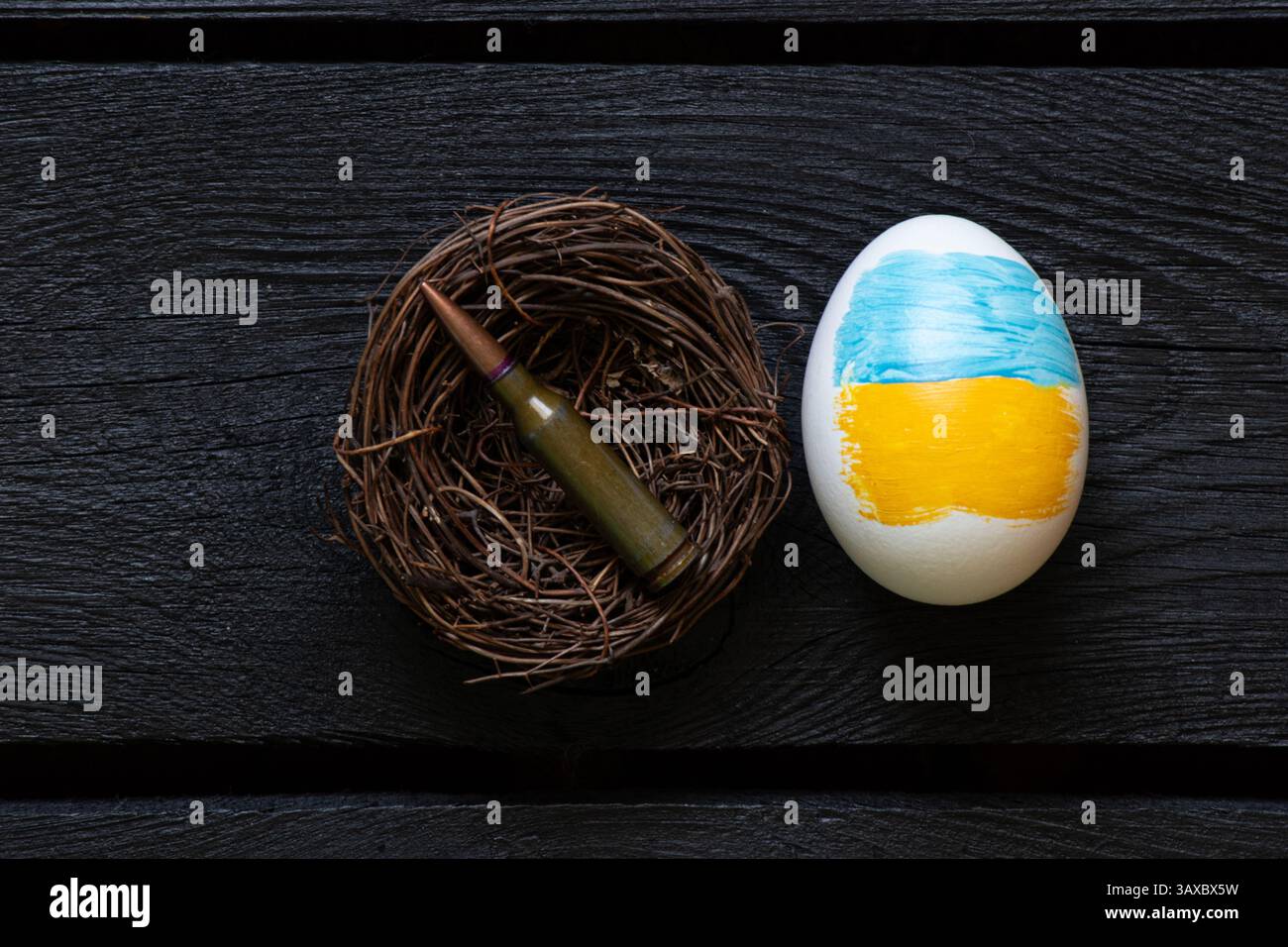 Ei mit Flagge der Ukraine und Kugel im Vogelnest auf schwarzem Brett, Krieg in der Ukraine und Ostern Stockfoto