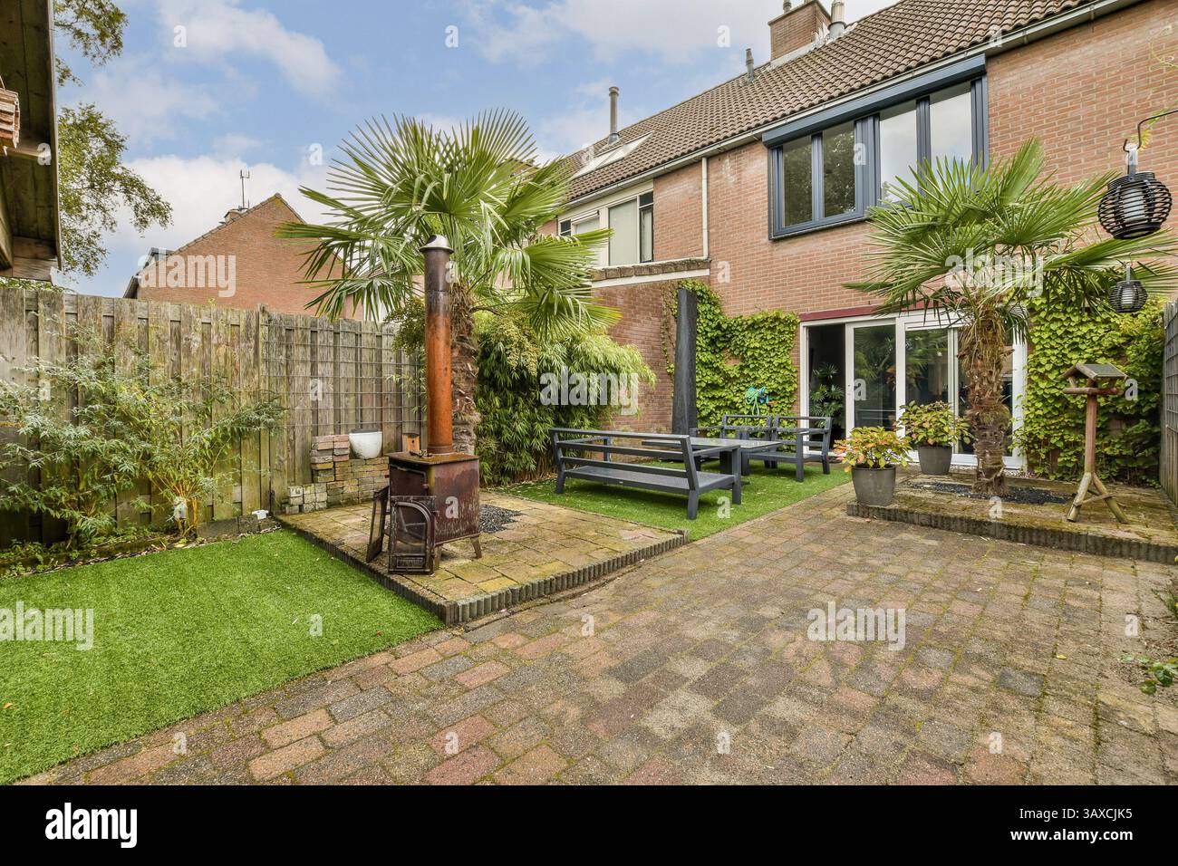 Eine ruhige Gartenszene mit üppigem Grün, einem gemütlichen Sitzbereich und Dekorationselementen im Freien, perfekt für Entspannung und Outdoor-Genuss. Stockfoto