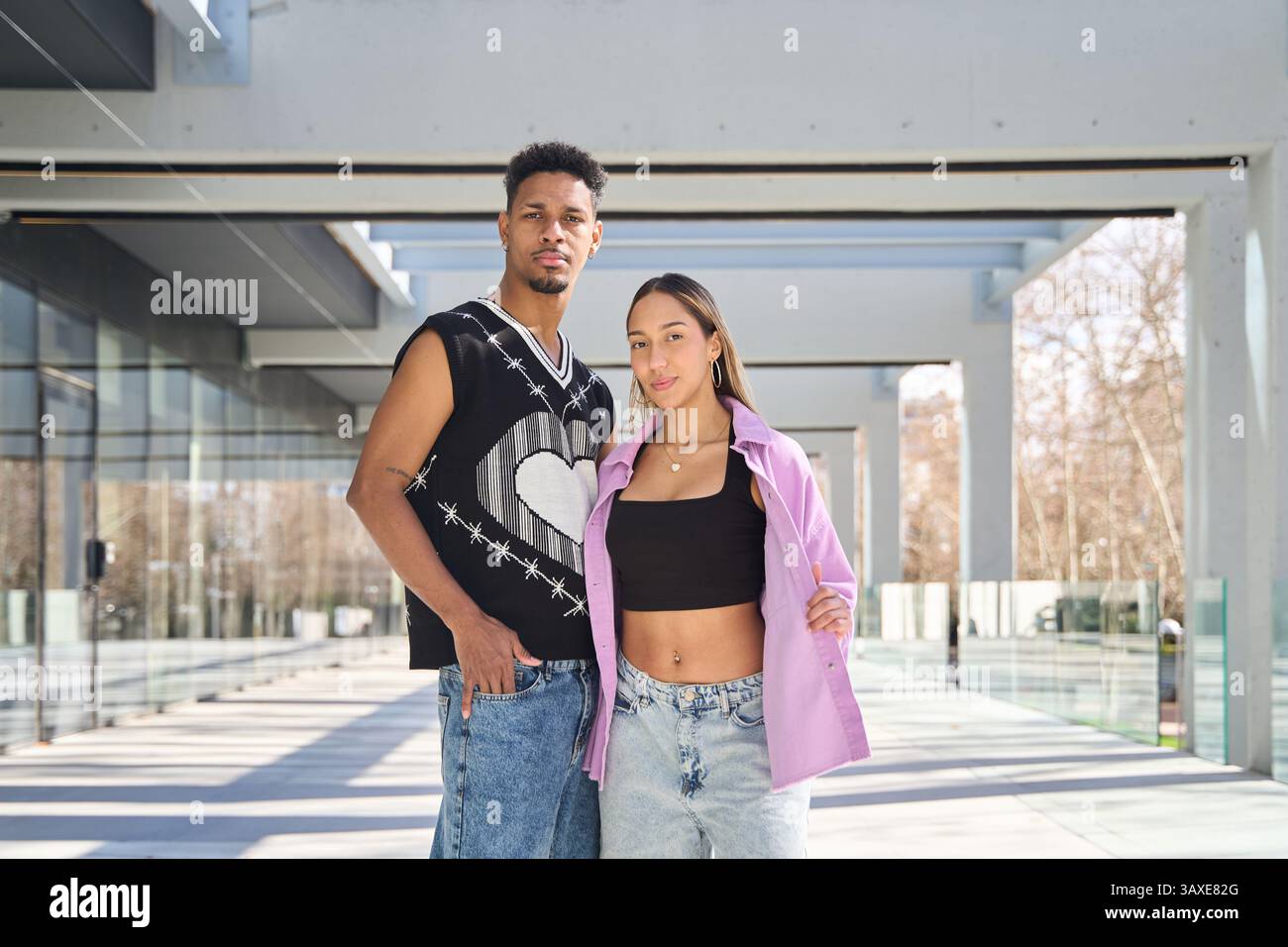 Stilvolle Tänzerinnen, die sich unter dem überdachten Gang eines modernen Gebäudes präsentieren, strahlen Selbstvertrauen und Freude in einer pulsierenden urbanen Umgebung aus Stockfoto