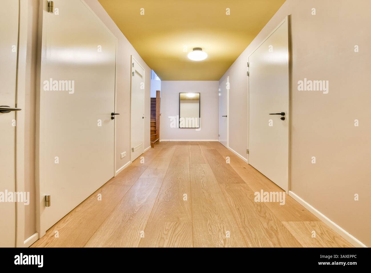 Ein geräumiger Flur mit klaren Linien, hellem Holzfußboden und neutralen Wänden, der zu einer Treppe führt und von einer zentralen Leuchte beleuchtet wird. Stockfoto