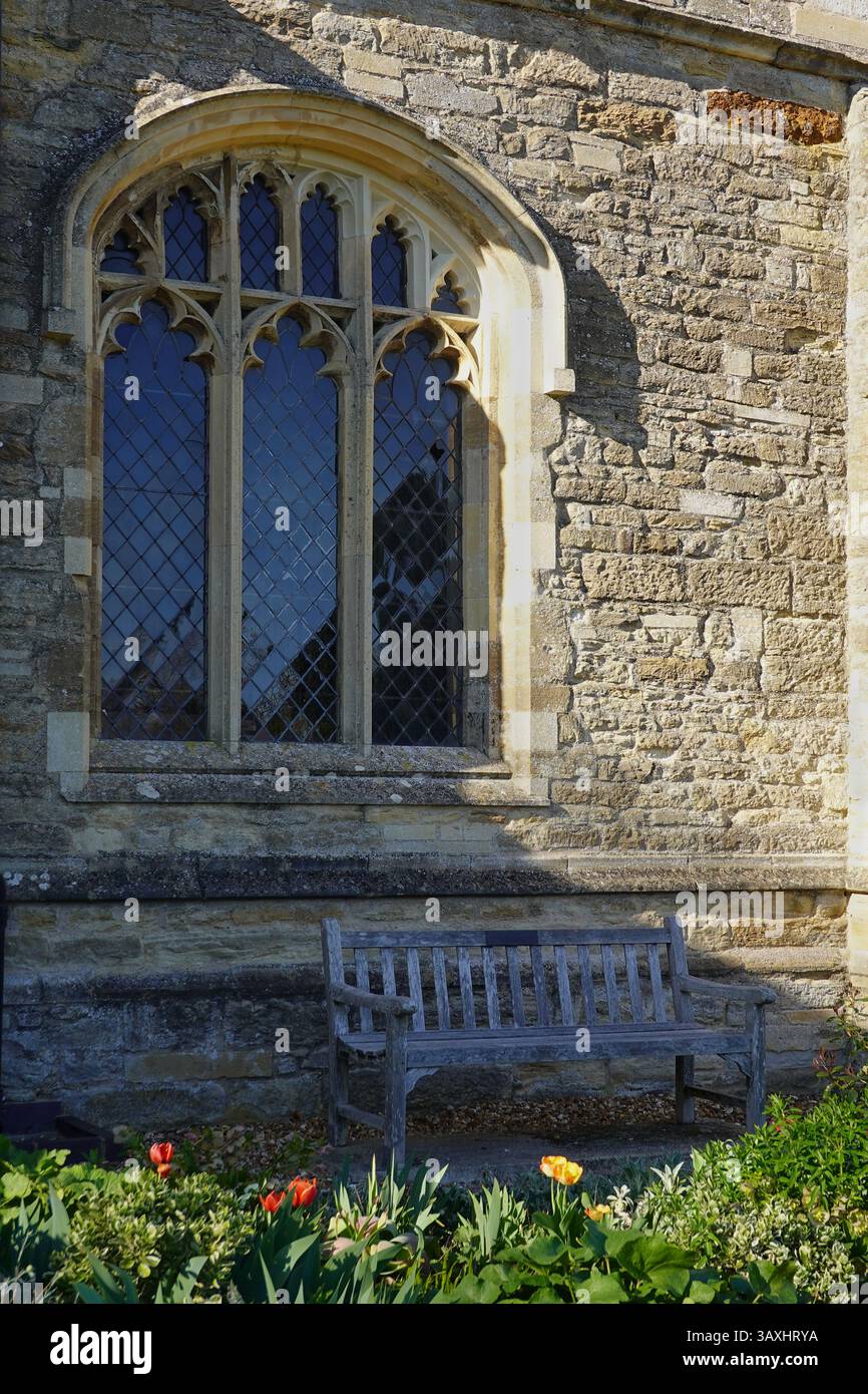 Sharnbrook, Bedfordshire, Großbritannien - Holzbank in ruhiger Lage an der St. Peter's Church auf der Südseite der Kirche mit farbenfrohen Blumen im Vordergrund Stockfoto