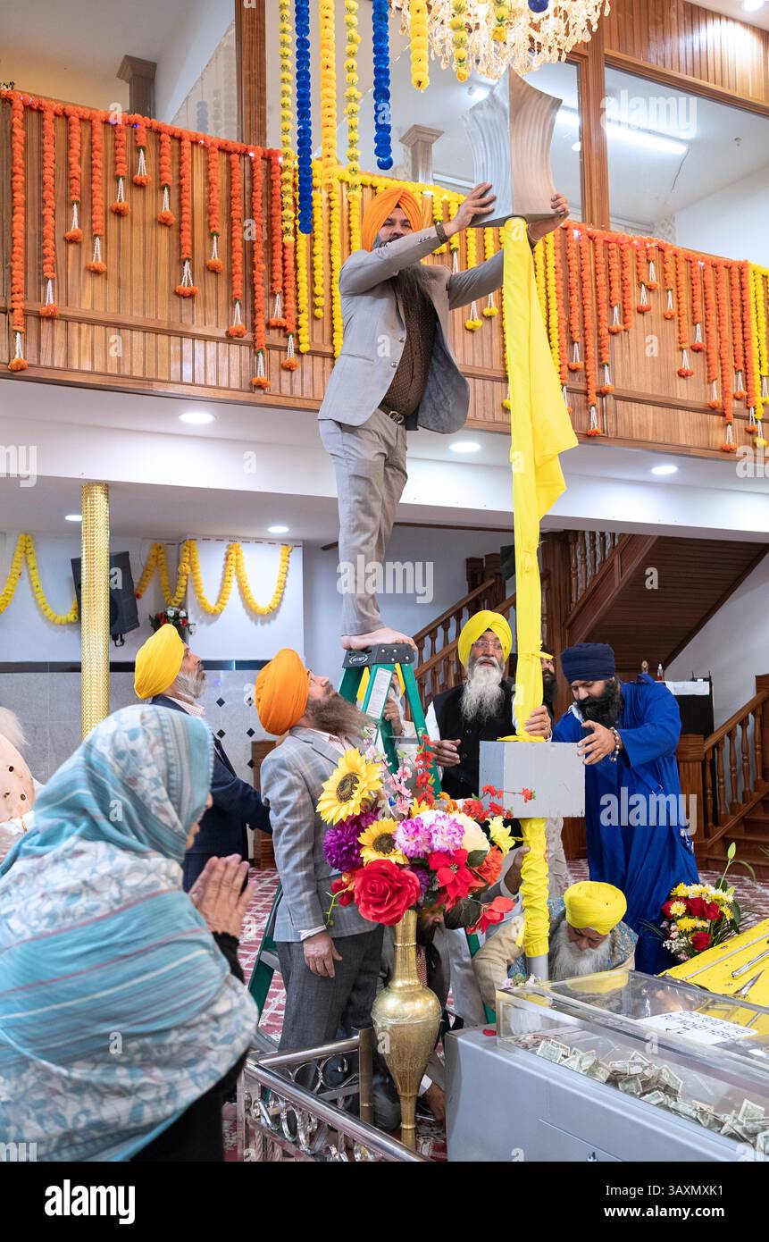 An Guru Nanaks Geburtstag ändern die Sikh-Anbeter die Stangen der Grant Sahib-Flagge. Im Baba Makhan Shah Lobana Sikh Center in Queens. Stockfoto