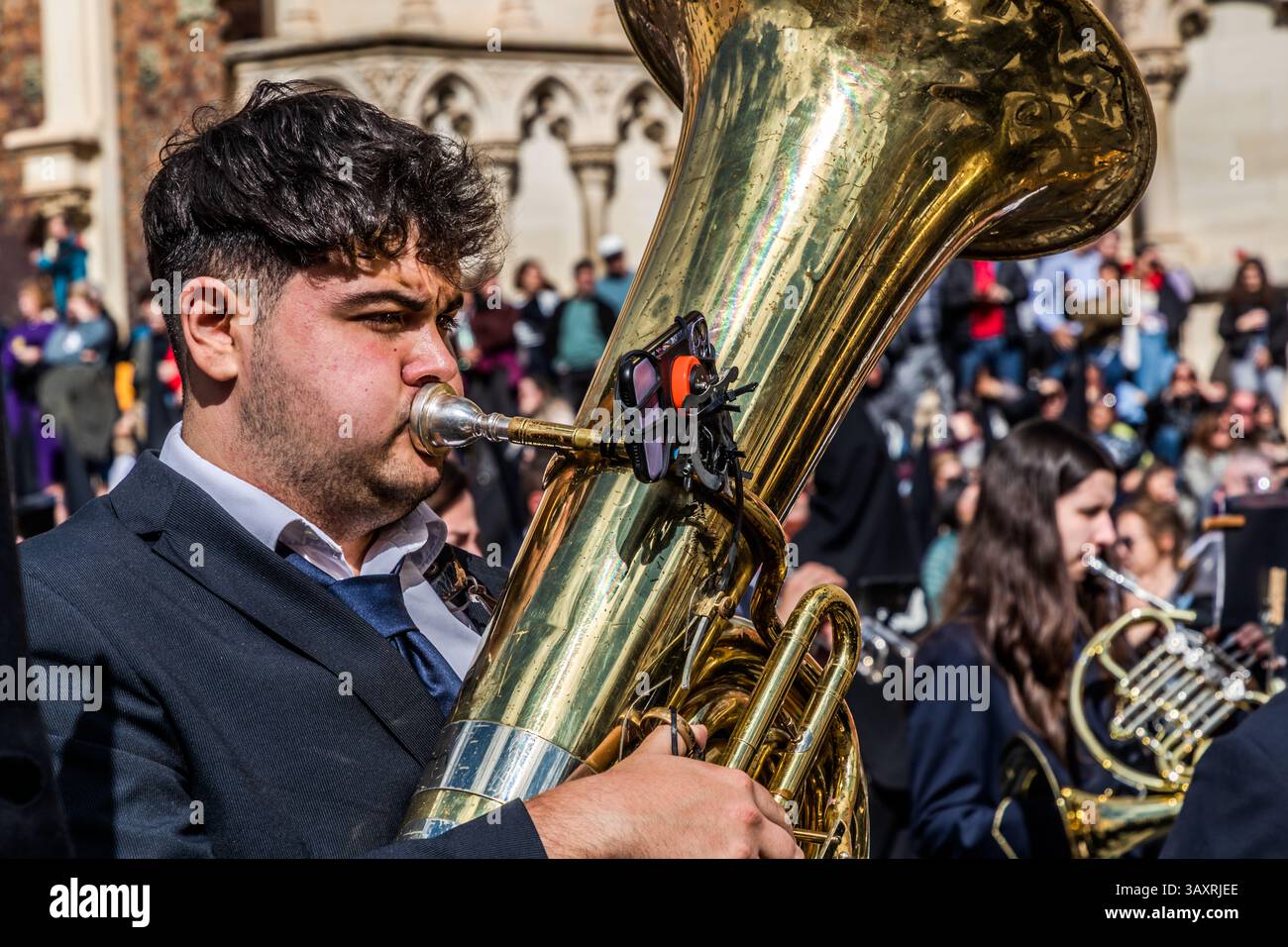 Karfreitagsprozession EN el Calvario in Cuenca. Ein junger Mann spielt die Tuba mitten in einer spanischen Musikgruppe und hat die Notizen auf seinem Smartphone Plaza Mayor, Cuenca, Castile-La Mancha, Spanien Stockfoto