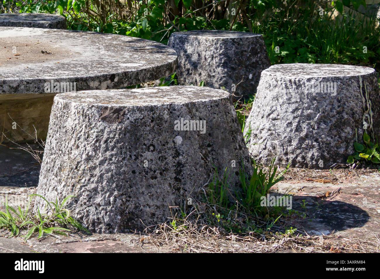 Ein einzigartiger Treffpunkt mit Steinbänken, die einen runden Tisch umgeben. Üppiges Grün und Sonnenlicht unterstreichen diese rustikale Umgebung im Freien, perfekt Stockfoto