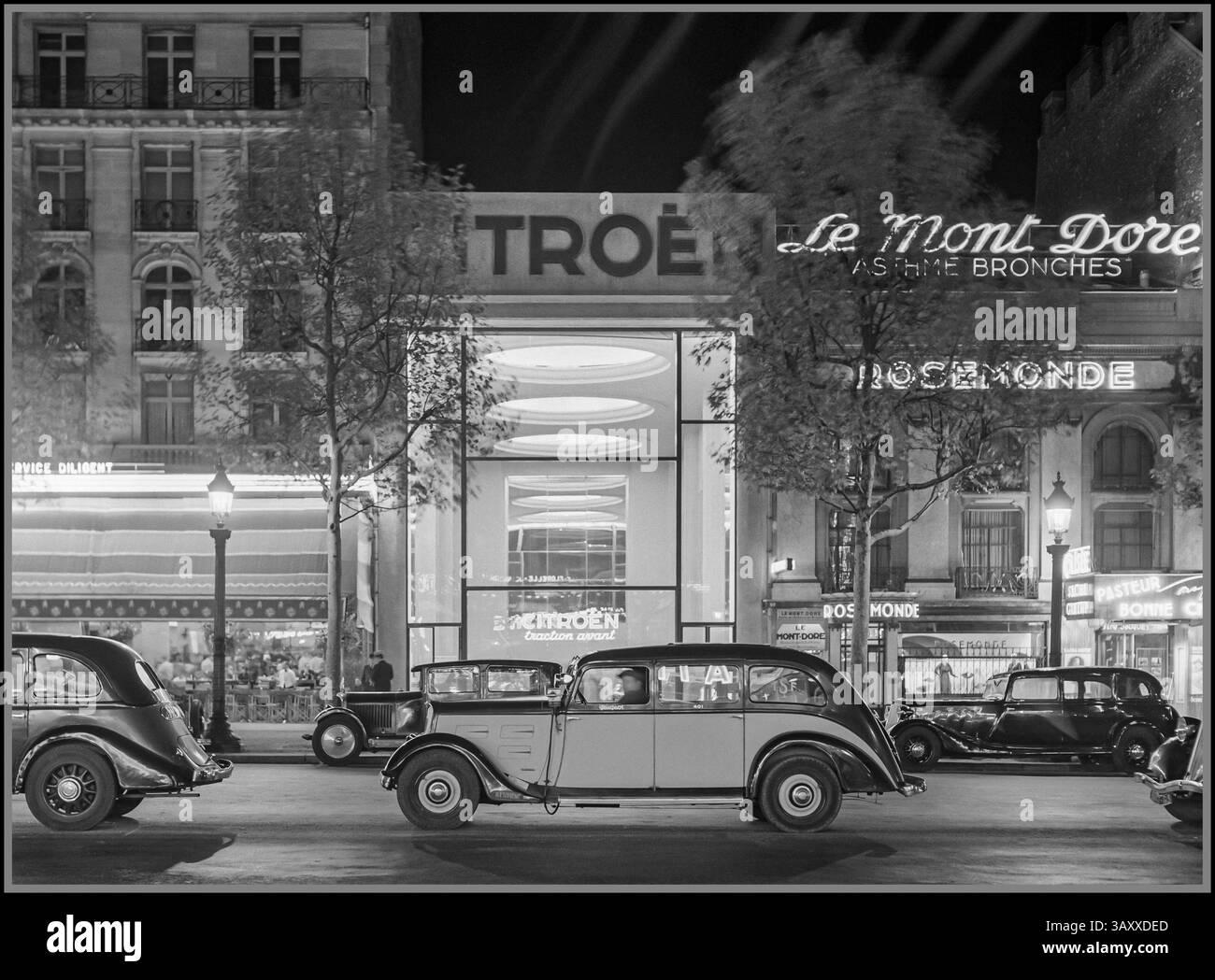 Klassische Pariser Straßenszene aus den 1930er Jahren bei Nachtwagen und Taxis auf den Champs-Elysées, mit dem beleuchteten Citroën-Showroom im Hintergrund, mit dem Peugeot-Taxi im Zentrum 1935 Paris-Stil Mode-Lifestyle der 1930er-Jahre vor dem Krieg Frankreich Stockfoto