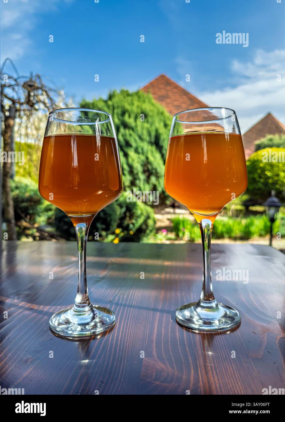 Erfrischende Getränke: Zwei volle Gläser im Freien an einem hellen Tag. Entspannender Nachmittag: Ein paar Drinks auf dem Patio-Tisch. Applaus. Zwei Stielgläser mit Col Stockfoto