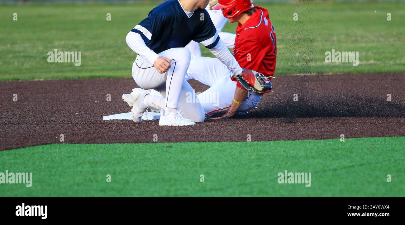 Baseballspieler, der die zweite Base klaut, schlägt den Wurf, den der zweite Baseman während eines High School-Spiels erwischt hat. Stockfoto