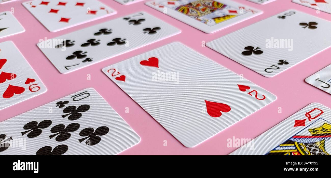 Sammlung von Spielkarten, die auf rosa Hintergrund angeordnet sind. Die Anzüge umfassen Herzen, Schläger und Diamanten. Die Karten sind leicht überlagert - Smartphone-aufgenommenes Stockfoto