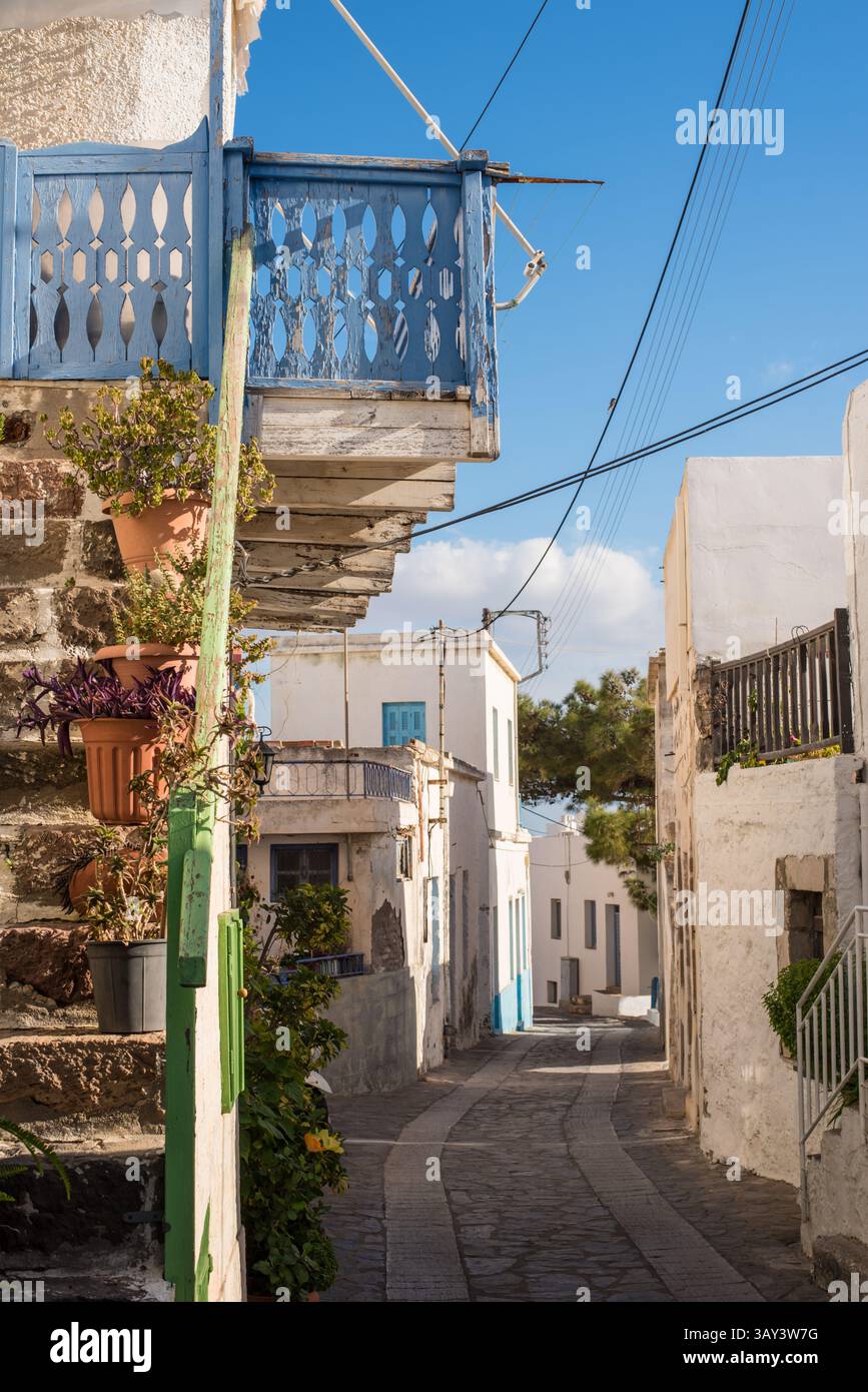 Sonnenbeschienene Gasse in Trypiti mit weiß getünchten Gebäuden mit blauen Akzenten, Topfpflanzen und einem ruhigen Himmel. Eine typisch griechische Inselszene auf Mi Stockfoto