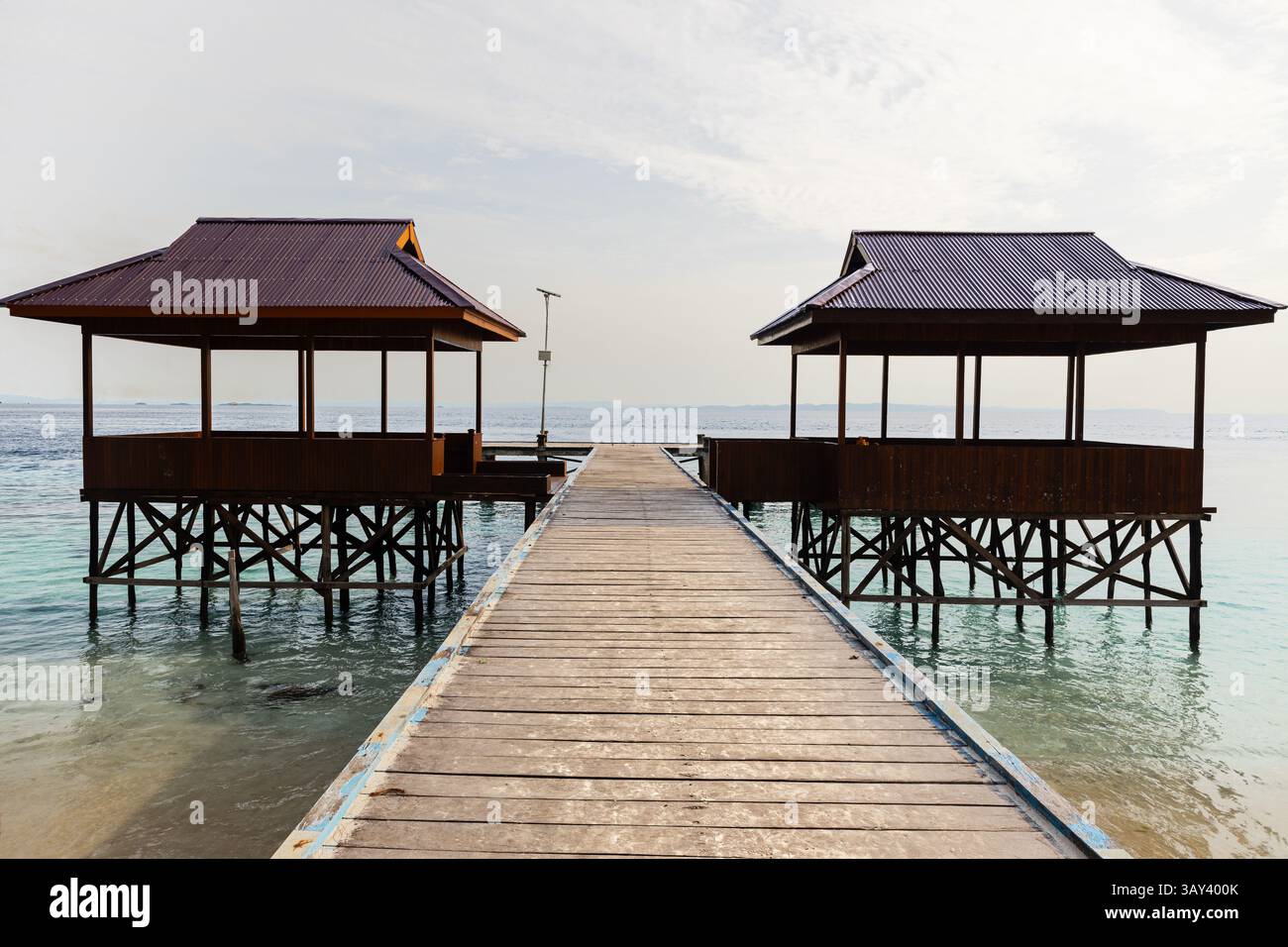 Blick von oben auf zwei traditionelle Überwasser-Pavillons, die durch einen Holzweg im unberührten Archipel von Raja Ampat verbunden sind und das klare türkisfarbene Wasser zeigen Stockfoto