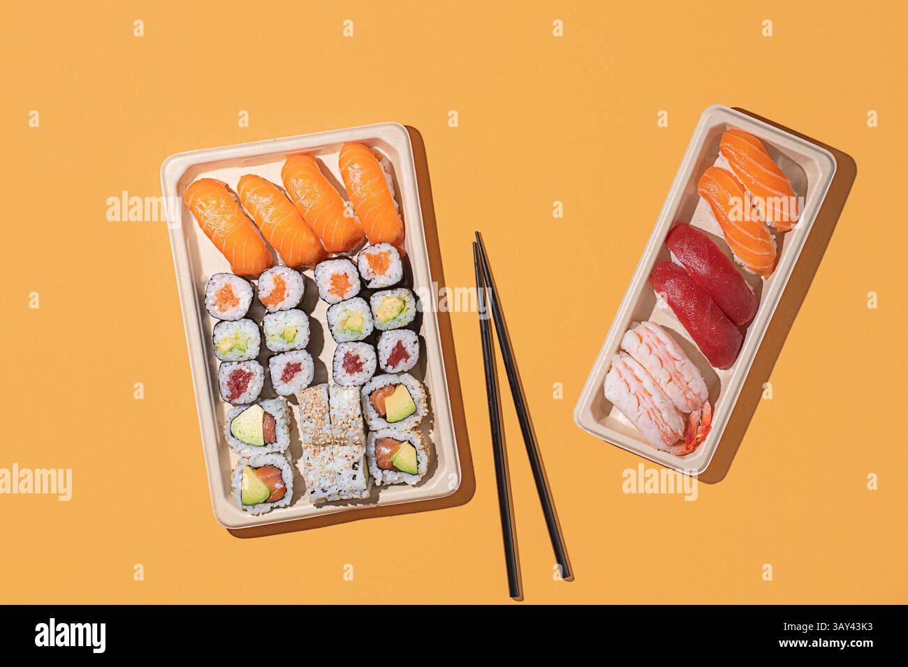 Minimalistischer Overhead-Sushi-Take-out-Boxen auf orangem Hintergrund mit Nigiri- und Maki-Rollen mit starker Richtungsbeleuchtung Stockfoto