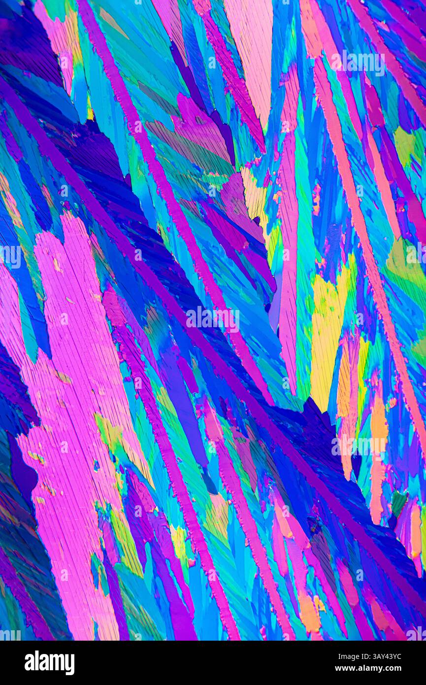 Lebendiges mikroskopisches Bild, das die kristalline Struktur der Adipinsäure zeigt, mit auffälligen Rosa-, Blau- und Grüntönen. Stockfoto