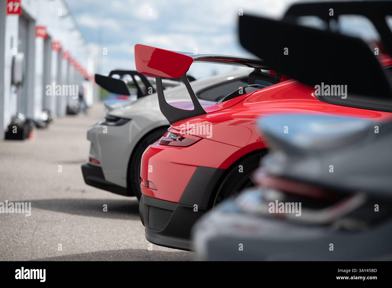 Eine Reihe von Hochleistungs-Sportwagen mit markanten Heckflügeln mit fortschrittlicher Aerodynamik und sportlichem Design, die entlang einer Rennstrecke geparkt werden. Stockfoto