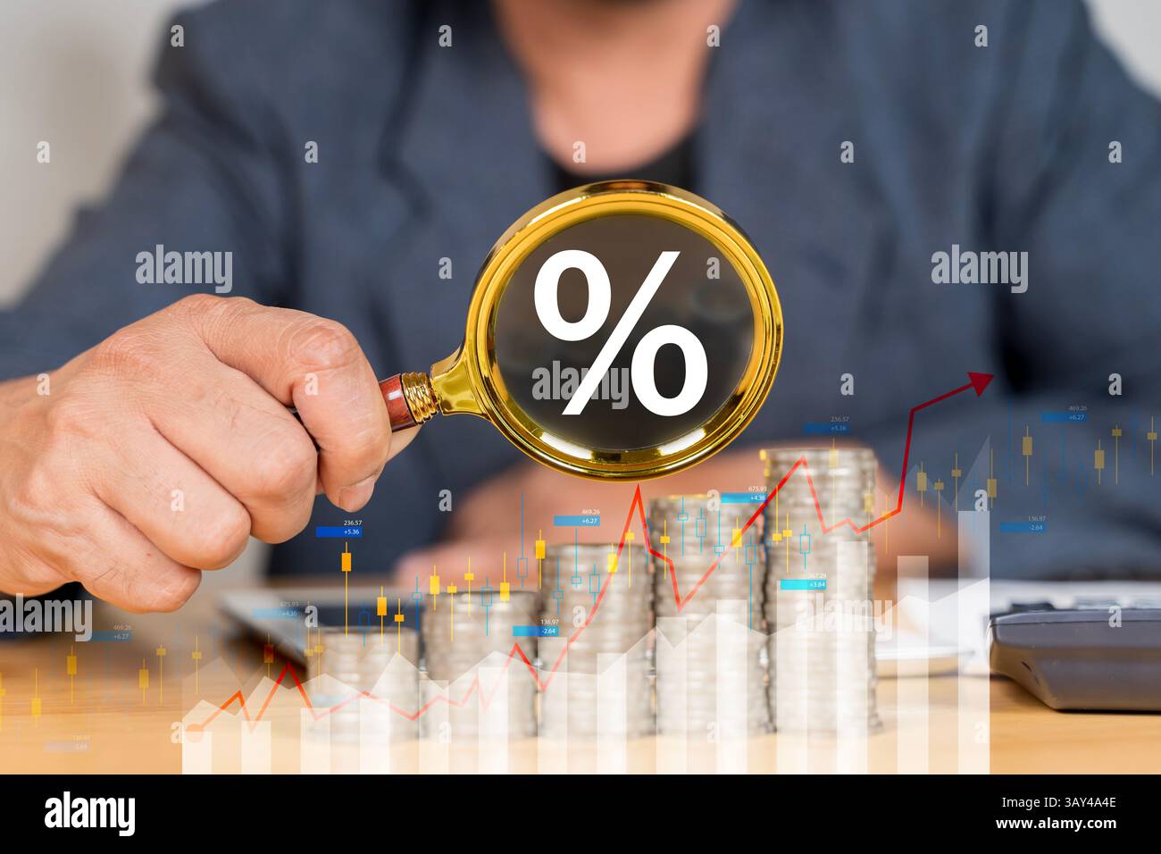 Ein Mann hält eine Lupe über einem Stapel Münzen. Die Münzen sind über den Tisch verstreut, und die Lupe wird verwendet, um sie zu untersuchen Stockfoto