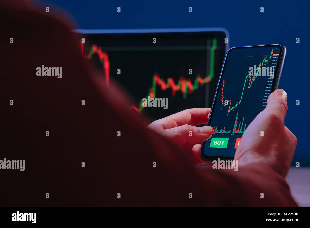 Trader hält ein Smartphone, verwendet die Trading-App zur Analyse von Finanz-, Börsen- und Kryptowährungsdaten, mit roten und grünen Kerzendiagrammen auf dem Bildschirm. Stockfoto