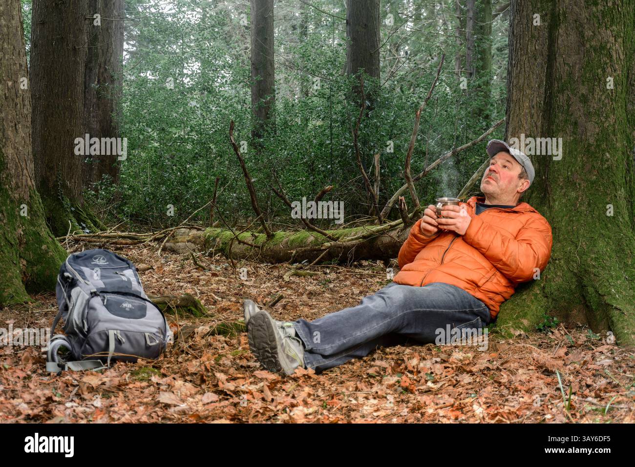 Ein Mann entspannt sich im Wald, umgeben von der Natur, und trinkt eine Tasse heißes Getränk – friedliche Momente im Wald. Stockfoto