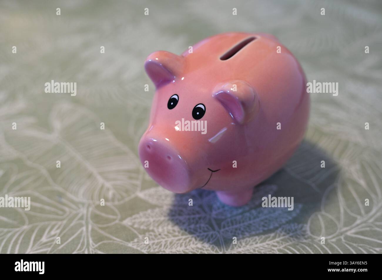 Ein rosafarbenes Schweinebett steht auf einer hellgrünen Tischdecke und lächelt Stockfoto