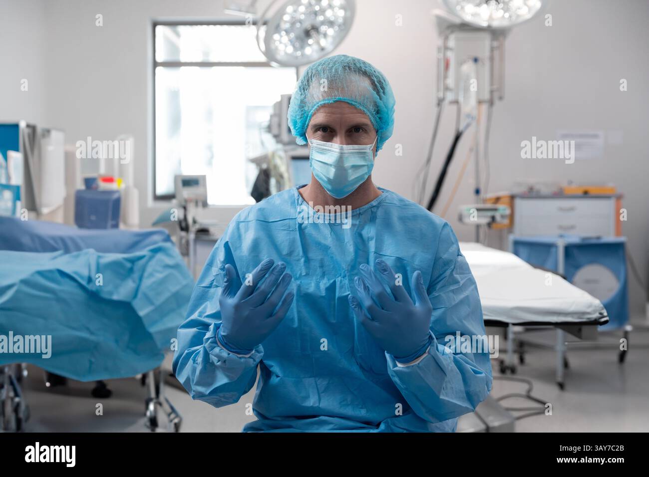 Männlicher Chirurg, der in der Mitte des Operationssaals steht, mit Deckenleuchten und Monitoren Stockfoto