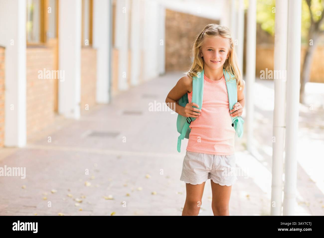 Ein Schüler, der über einen überdachten Schulflur läuft, einen mintgrünen Rucksack trägt, einen Kopierraum Stockfoto