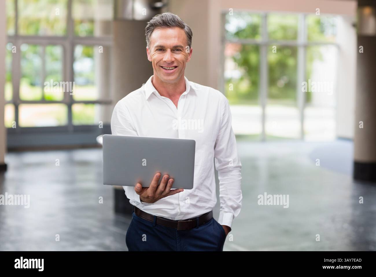 Reifer Erwachsener mit Laptop in der modernen Bürolobby, mit poliertem Boden und Grün Stockfoto