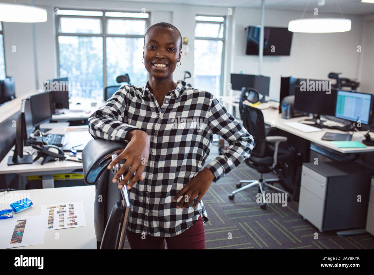 Afroamerikanische Frau lehnt sich auf ergonomischen Stuhl im Großraumbüro mit Monitoren und Fotos Stockfoto