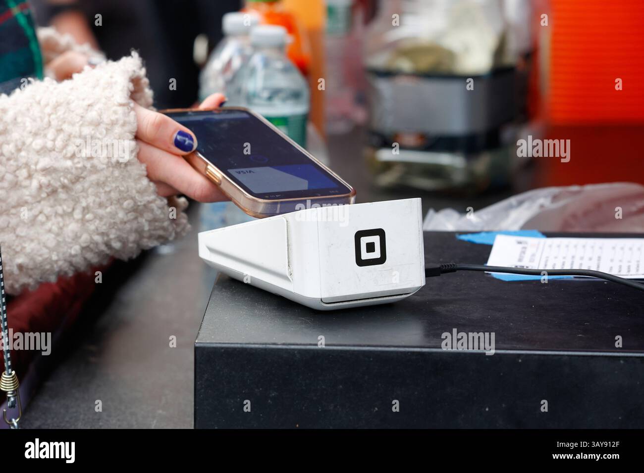 Eine Person hält ein Smartphone über ein drahtloses Square Terminal Point of Sales-Gerät, um eine NFC-mobile Zahlung oder kontaktlose digitale Zahlung zu tätigen. Stockfoto Eine Person hält ein Smartphone über ein drahtloses Square Terminal Point of Sales-Gerät, um eine NFC-mobile Zahlung oder kontaktlose digitale Zahlung zu tätigen. Stockfoto