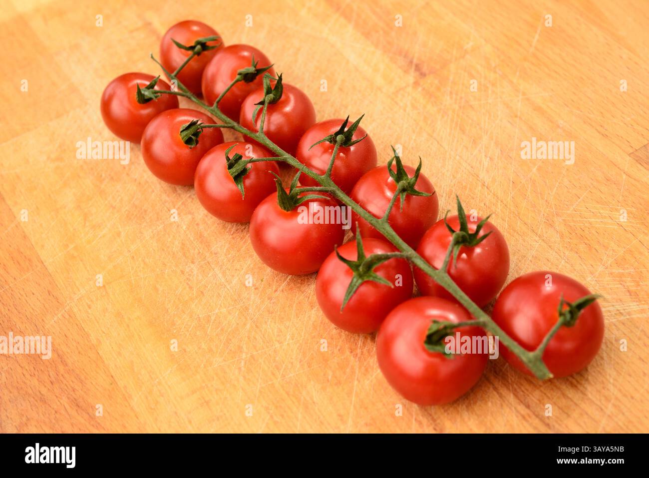 Reife rote Kirschtomaten auf der Rebe, Holzoberfläche, Bio-Tomaten, Gourmet-Küche, Weintomaten Stockfoto