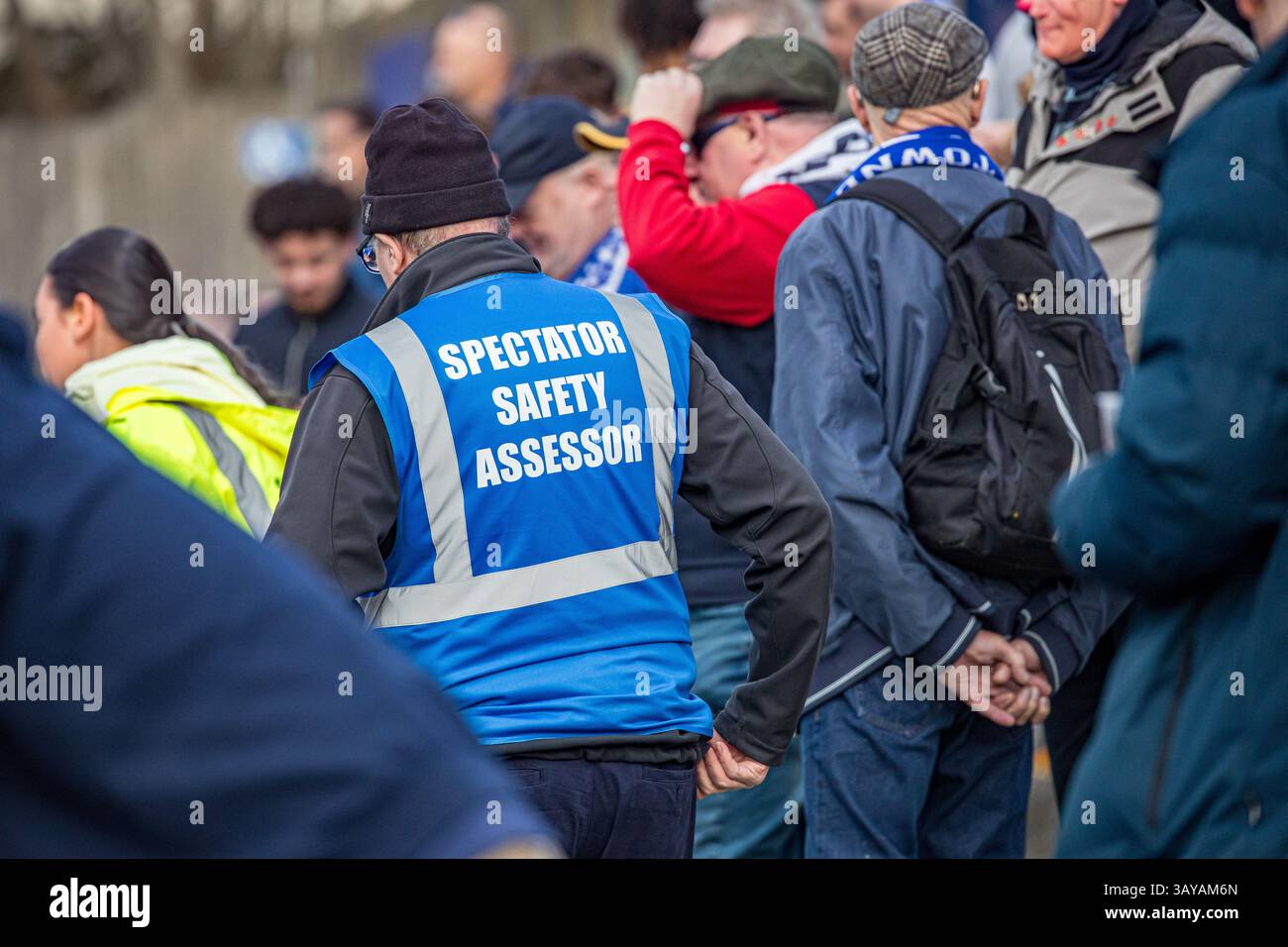 Zuschauersicherheitsbewerter, der bei einem Fußballspiel in einer blauen, gut sichtbaren Jacke durch die Massen der Fans läuft Stockfoto