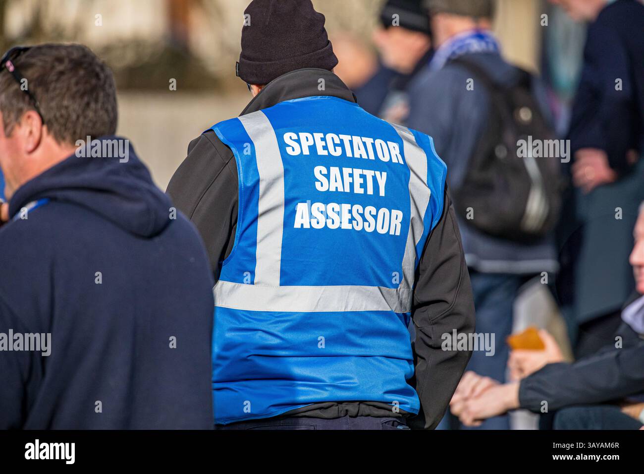Zuschauersicherheitsbewerter, der bei einem Fußballspiel in einer blauen, gut sichtbaren Jacke durch die Massen der Fans läuft Stockfoto