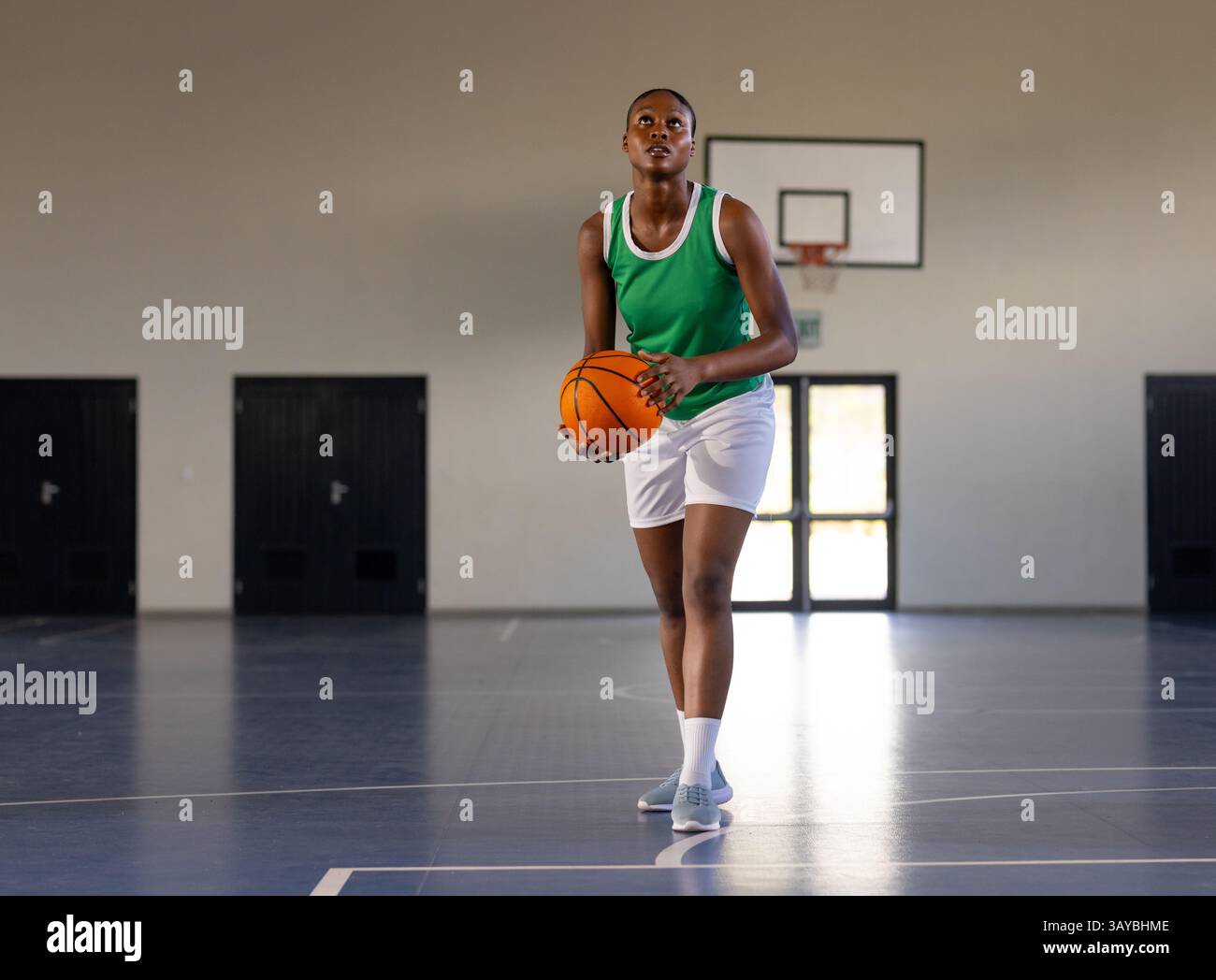 Afroamerikanerin, die Basketball hält, zielt auf ein Basketballfeld mit Korb, Türen Stockfoto