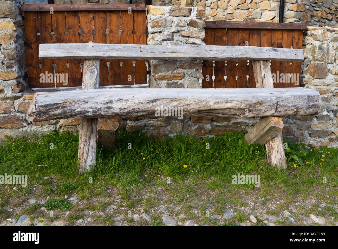 Alte traditionelle Bank aus Holz vor einem Stein und Holzzaun auf dem Land Stockfoto