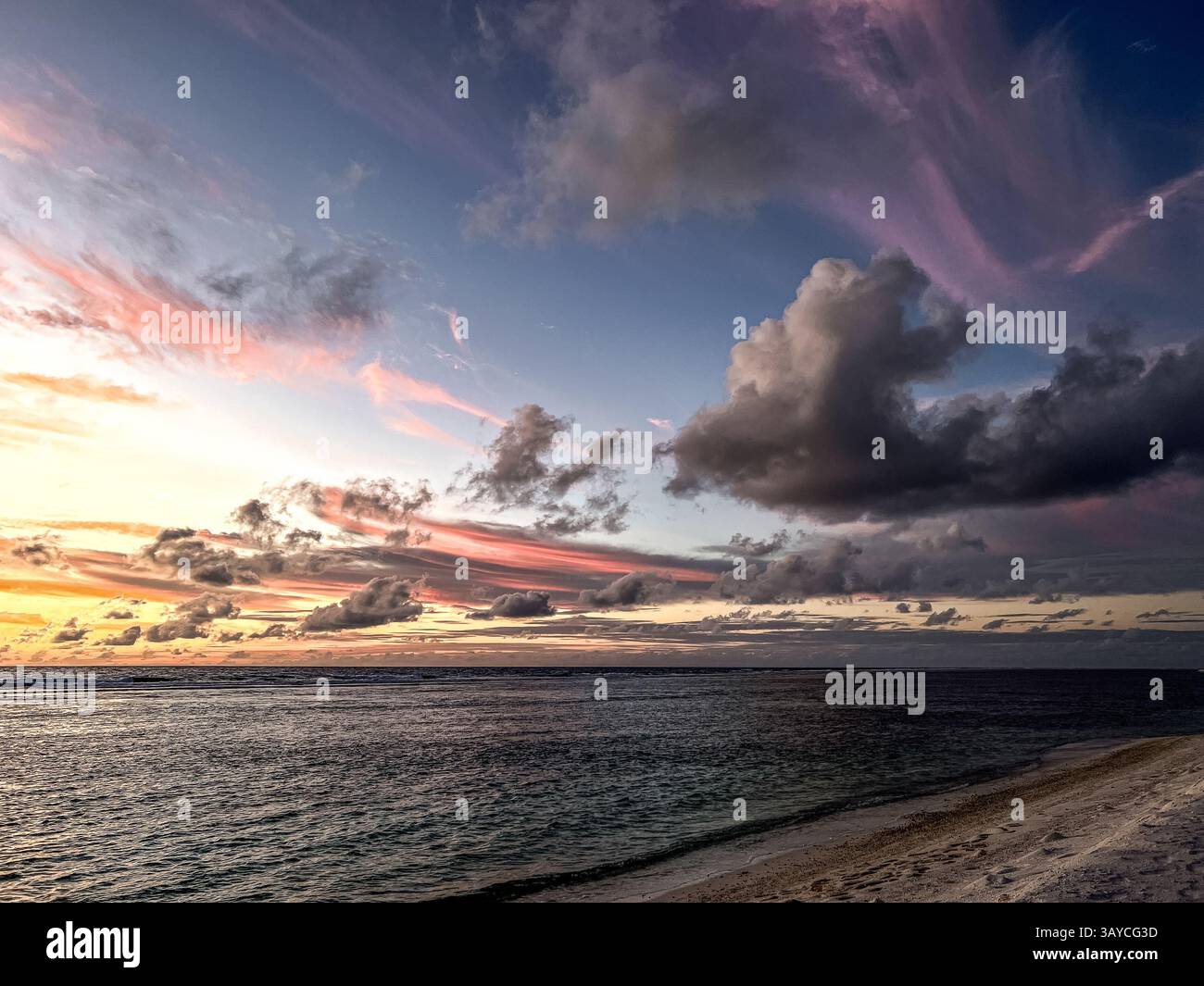 Atemberaubender Sonnenuntergang über dem Meer, wo leuchtende Farben über den Himmel tanzen und sich auf dem ruhigen Wasser unter Ihnen spiegeln. Die dramatischen Wolken sorgen für Tiefe Stockfoto