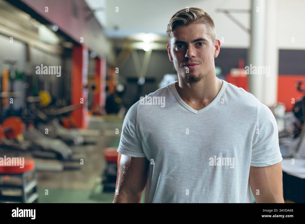 Sportlicher Mann, der im modernen Fitnessraum steht, mit Bänken, Hantelständern und Hocketständer Stockfoto