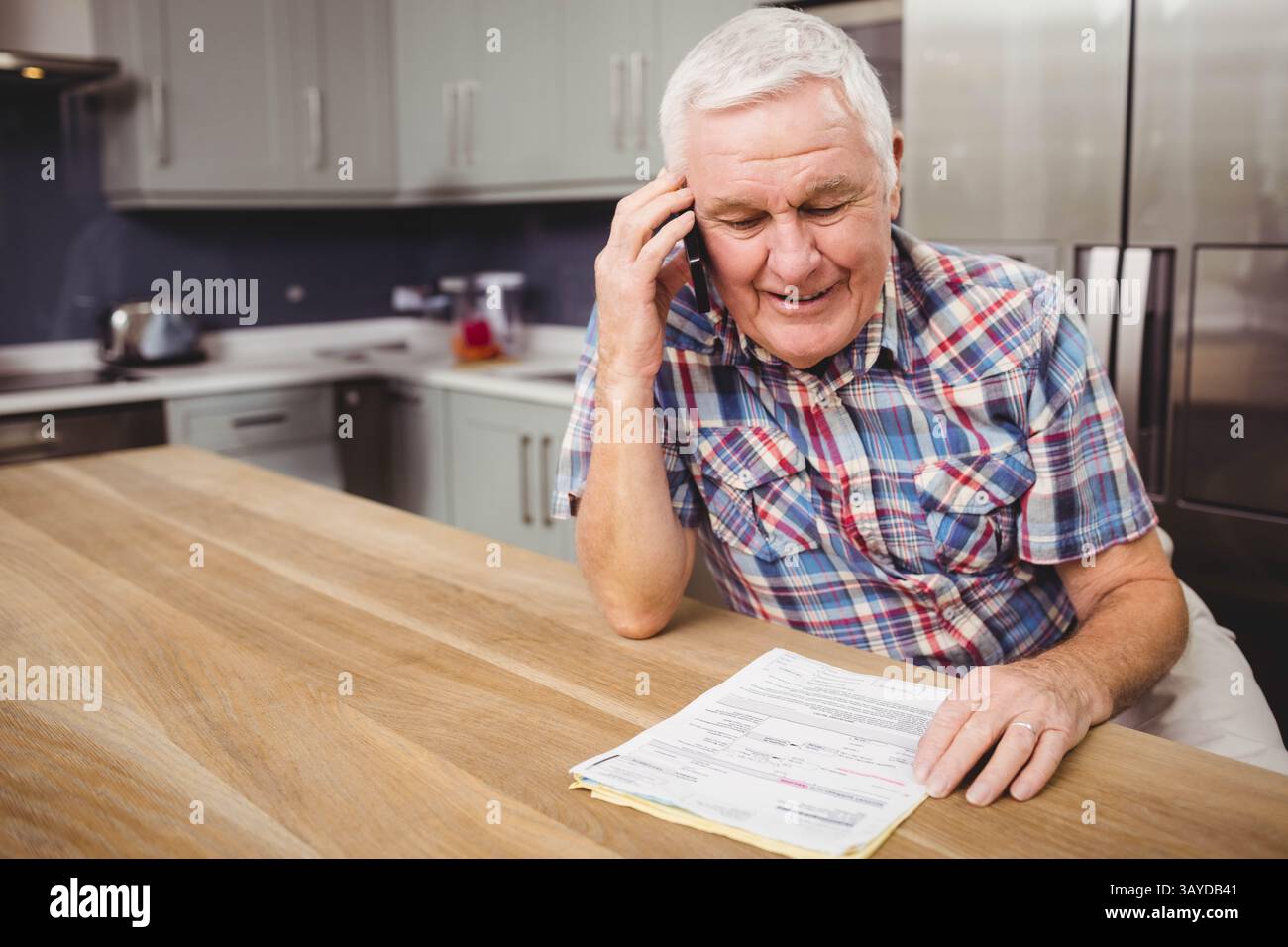 Senior Mann, der mit dem Smartphone spricht, auf einer Holzinsel in der Küche, im Kopierraum Stockfoto