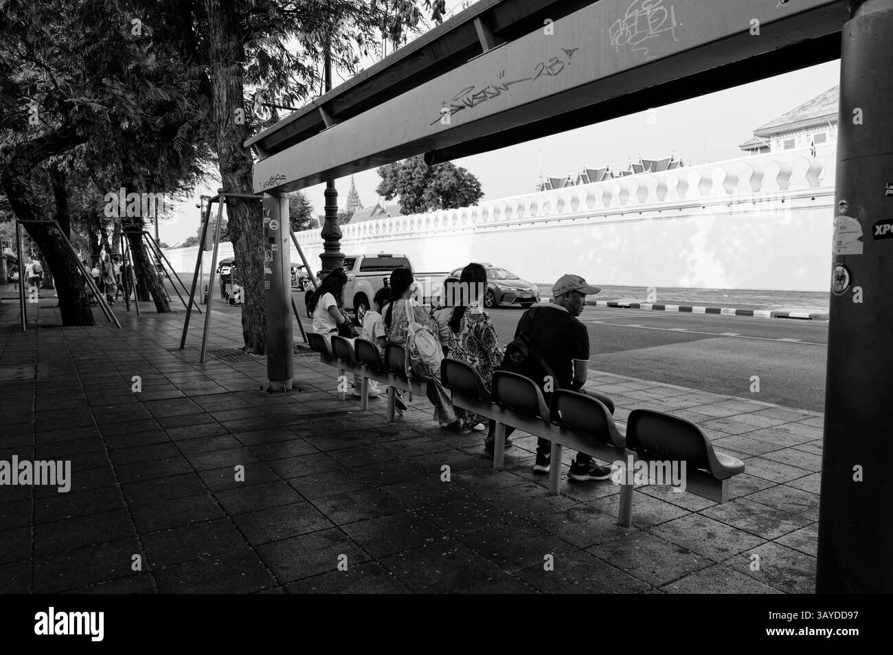 Einheimische und Touristen sitzen in ruhiger Erwartung an einer schattigen Bushaltestelle vor der Mauer des Großen Palastes Stockfoto